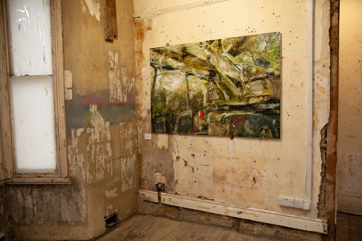 A decaying military-green crane or heavy machinery vehicle sits partially buried in a woodland clearing, its massive hydraulic arms rusted and streaked with oxidised residue. Autumnal foliage surrounds and overlays the scene, while painterly textures and ghosted transparencies give the piece a spectral, timeworn atmosphere. A solitary red fuel container adds a flash of colour against the muted industrial palette.