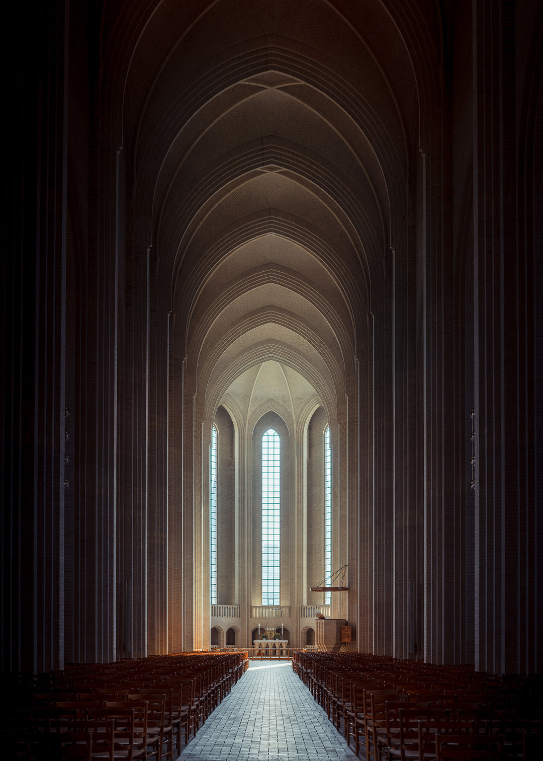 Panoramic photograph of Grundtvigs Kirke interior, showing soaring brick arches, vertical symmetry, tall windows and glowing light, capturing the calm geometry and spiritual presence of Danish Brick Expressionism.