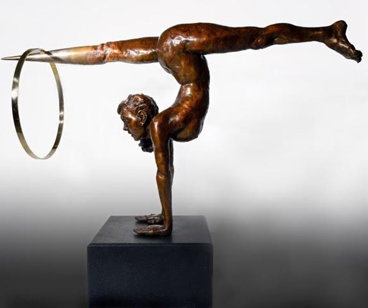 Teresa Wells’ Viktoriya (2018), limited edition bronze and brass sculpture on granite, portraying a powerful female acrobat in a one-armed handstand with legs extended horizontally, one foot tapering into a polished brass point that pierces a large brass hoop. The patinated bronze figure features finely modelled musculature, braided hair, and a dynamic forward gaze, balancing strength and grace. Mounted on a solid black granite base, the 100cm×30cm×50cm, 73kg piece is designed for impactful indoor display.