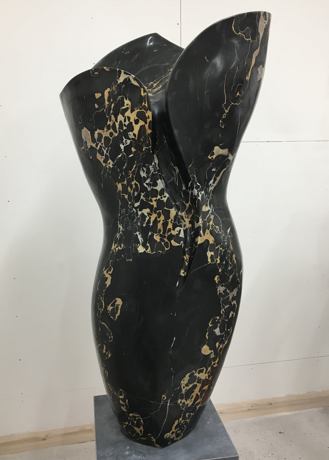 Large contemporary sculpture carved from luxurious Portoro marble, its tall, feminine form flowing with soft curves and dramatic black surface veined with striking gold and ivory patterns, standing on a solid stone plinth.
