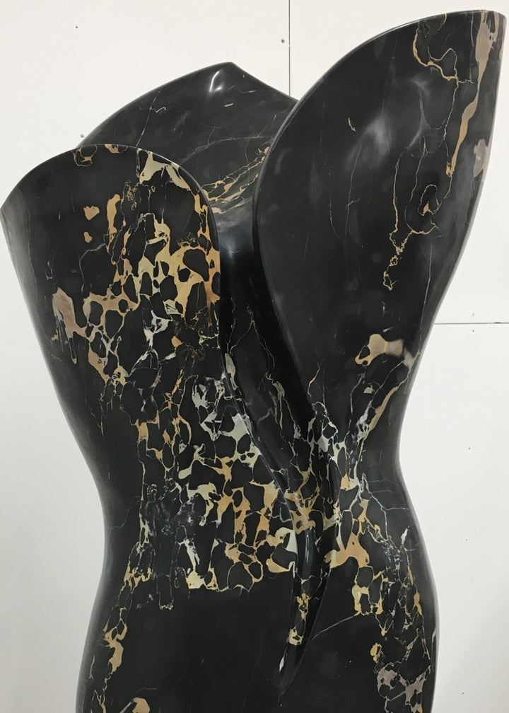 Large contemporary sculpture carved from luxurious Portoro marble, its tall, feminine form flowing with soft curves and dramatic black surface veined with striking gold and ivory patterns, standing on a solid stone plinth.