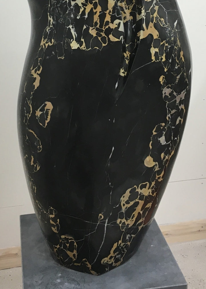 Large contemporary sculpture carved from luxurious Portoro marble, its tall, feminine form flowing with soft curves and dramatic black surface veined with striking gold and ivory patterns, standing on a solid stone plinth.