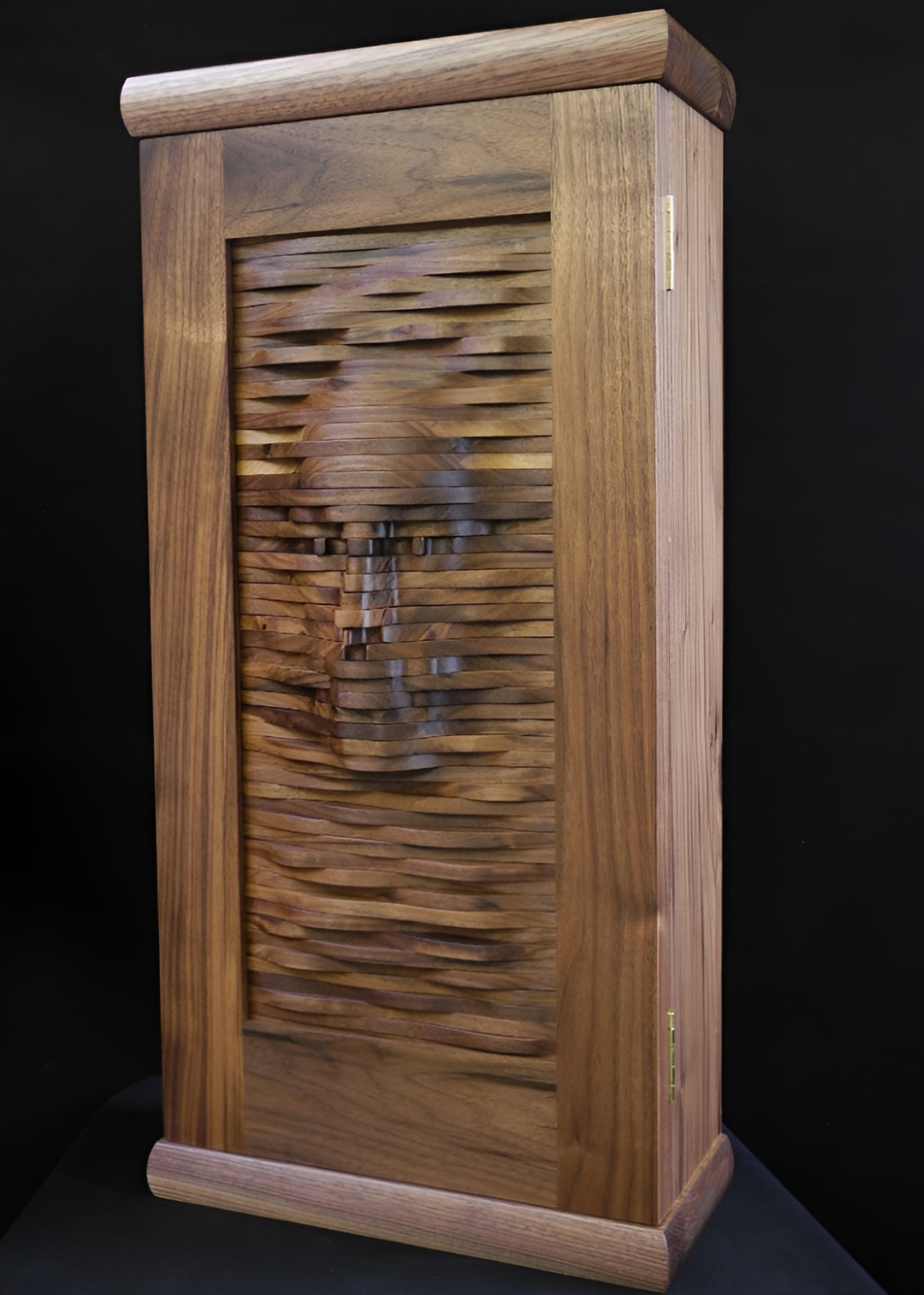 Handcrafted walnut cabinet with a sculpted front panel, its layered wooden surface forming the impression of a human face emerging from rhythmic carved waves.