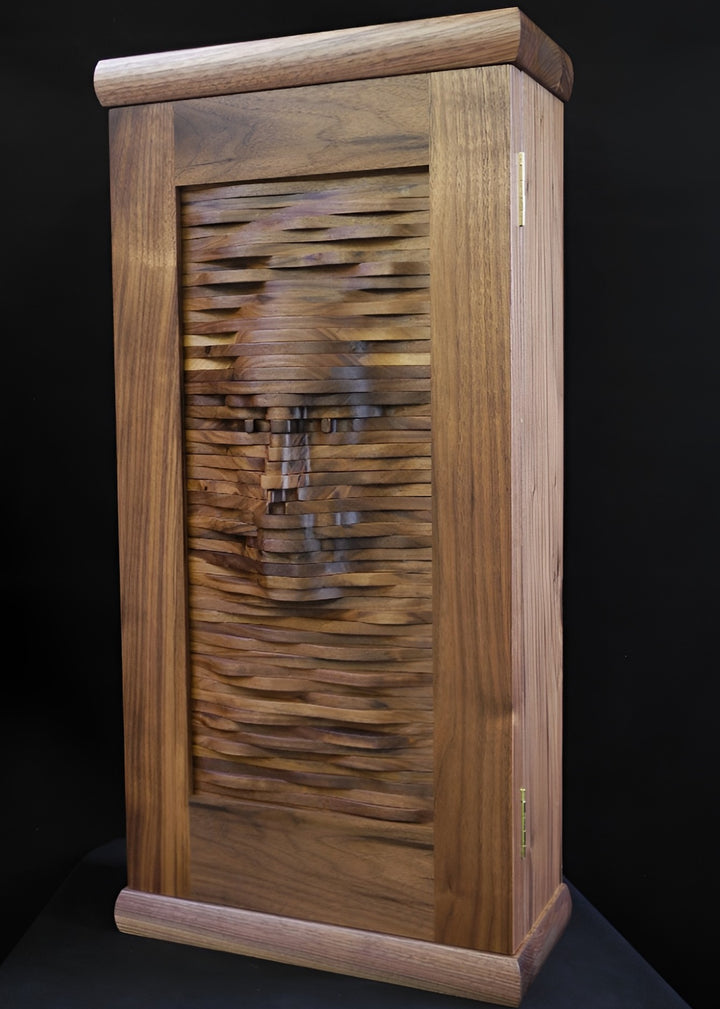 Handcrafted walnut cabinet with a sculpted front panel, its layered wooden surface forming the impression of a human face emerging from rhythmic carved waves.