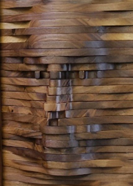 Handcrafted walnut cabinet with a sculpted front panel, its layered wooden surface forming the impression of a human face emerging from rhythmic carved waves.
