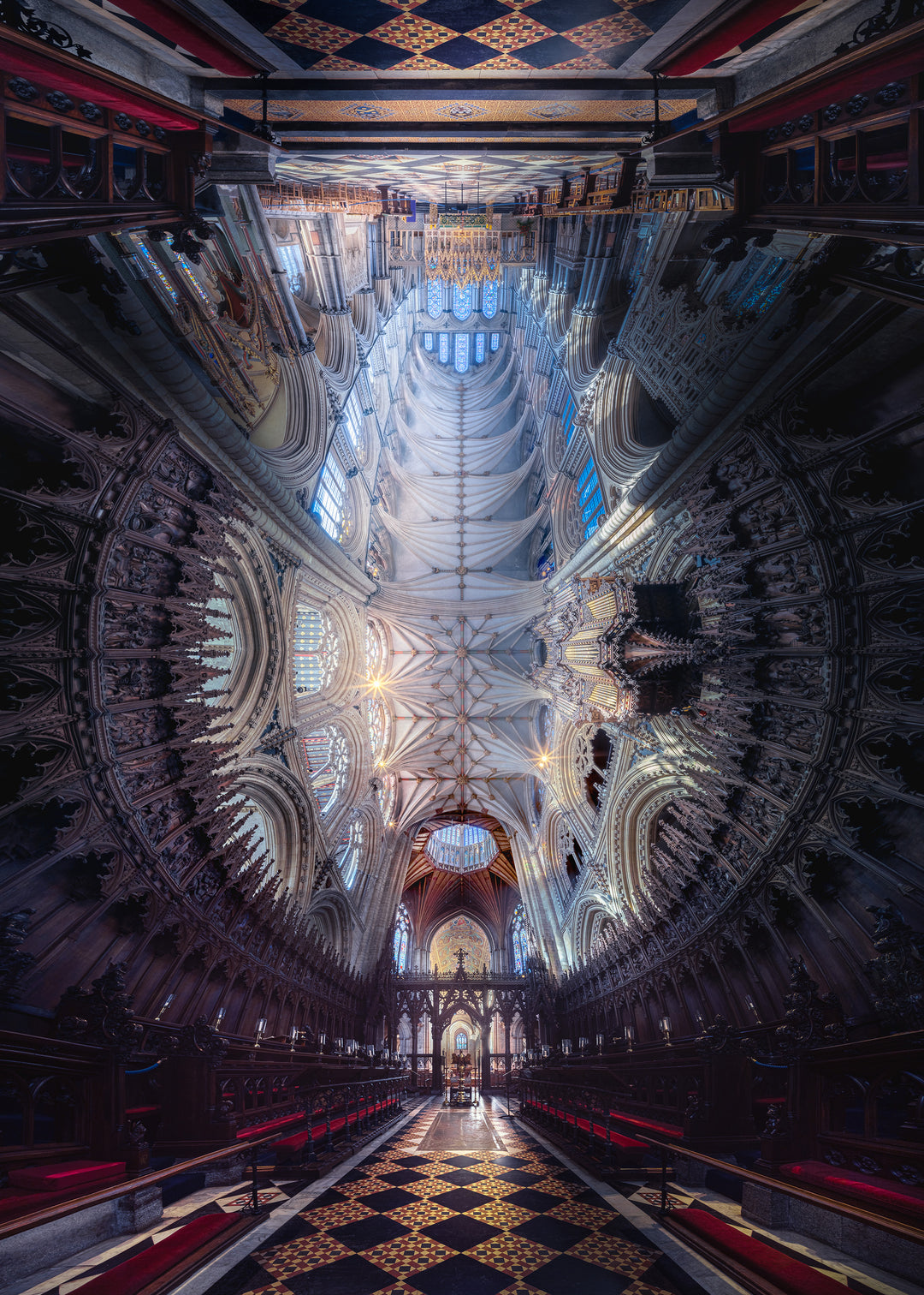 Panoramic photograph of Ely Cathedral interior, showing the soaring nave, intricate fan vaulting, and dramatic symmetry, blending Romanesque and Norman architecture with light, colour, and choral presence.