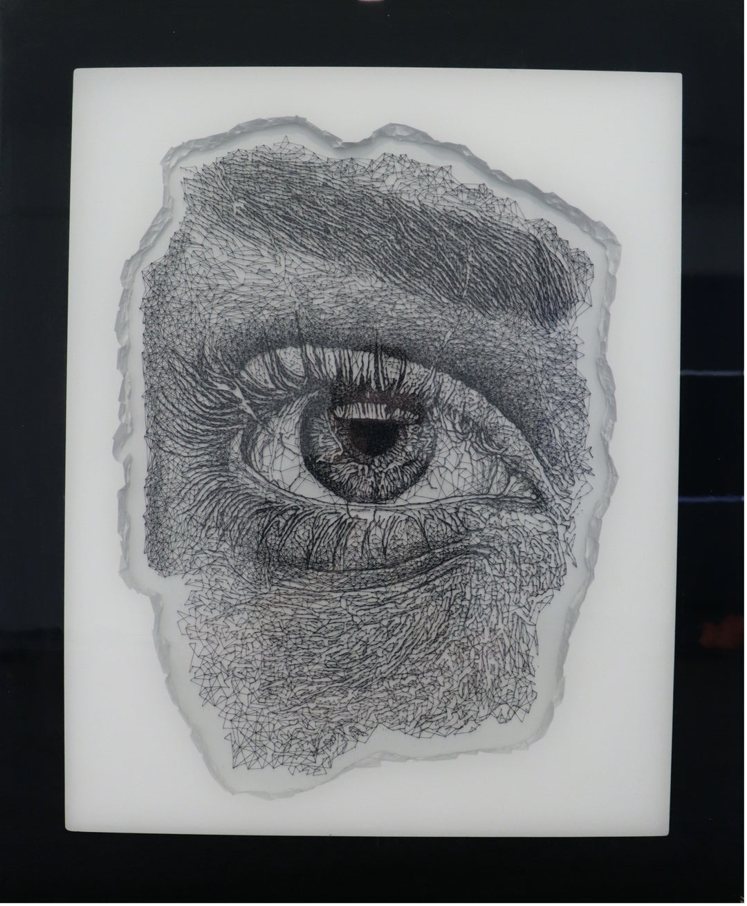 Hyperrealistic string art composition of a human eye, meticulously crafted with 9,200 pins and 200 metres of black string on a white fractured-edge acrylic panel, set against a glossy black background. The monochromatic detail highlights fine textures of lashes, iris, and skin.