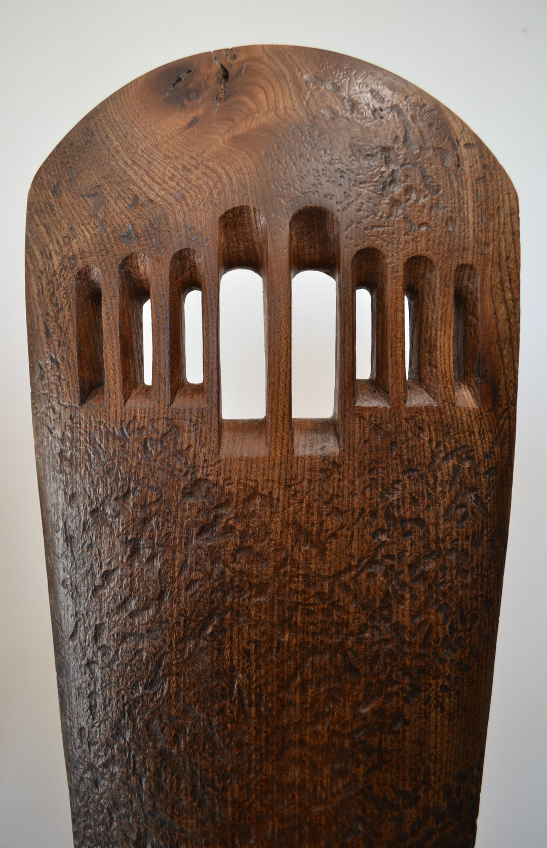 “Visori” by Nicola Beattie – a tall elm sculpture on an oak base, hand-carved with textured surface and visor-like openings. Part of her Blade series, it symbolises endurance, conflict, and the emergence of light from darkness.
