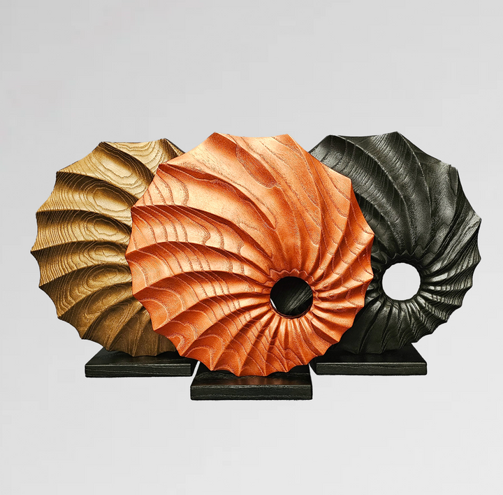 Trio of carved wood sculptures in gold, copper, and black finishes with spiral textures and central circular voids on black bases.
