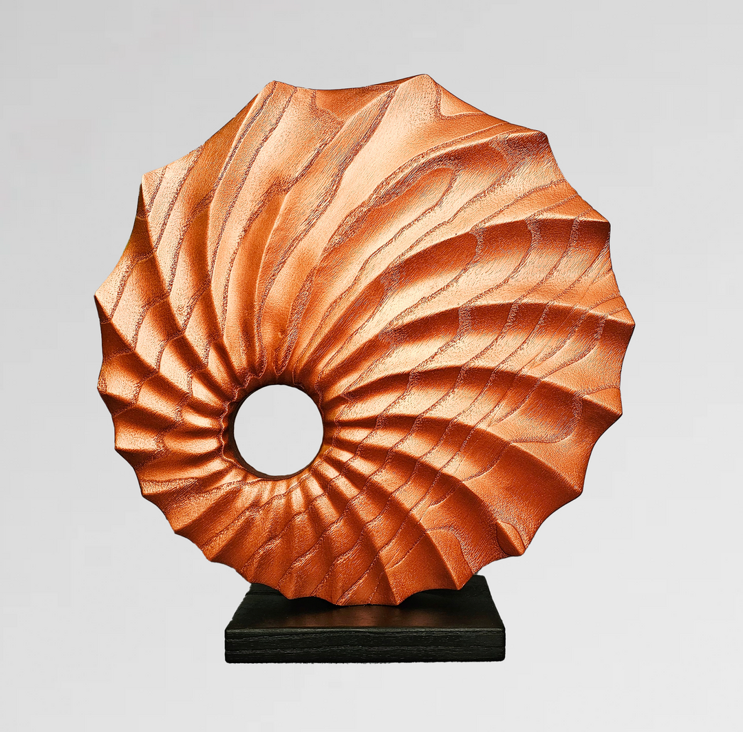 carved wood sculpture in gold finish with spiral textures and central circular voids on black base.
