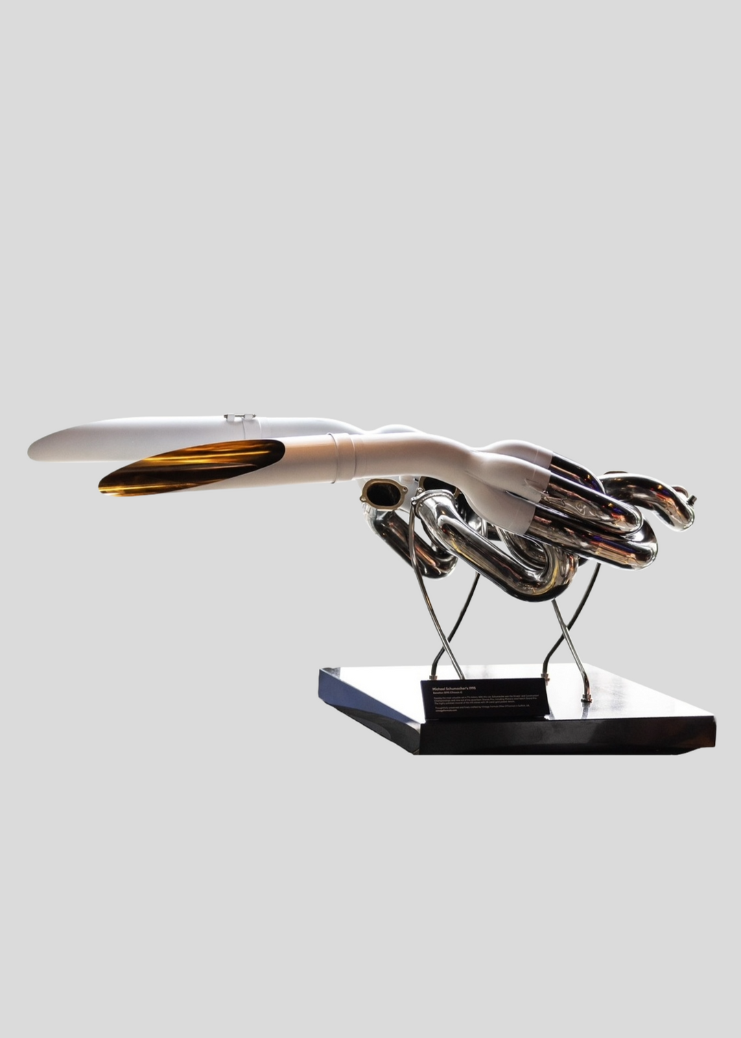 Highly polished sculptural artwork by Mike O’Connor crafted from the authentic race-used exhaust system of Michael Schumacher’s 1995 Benetton B195 Formula One car. The piece features flowing Inconel and stainless-steel pipes with mirror-finished chrome surfaces and 24-karat gold interior detailing, mounted on a sleek stand. A striking one-of-one collector’s piece 