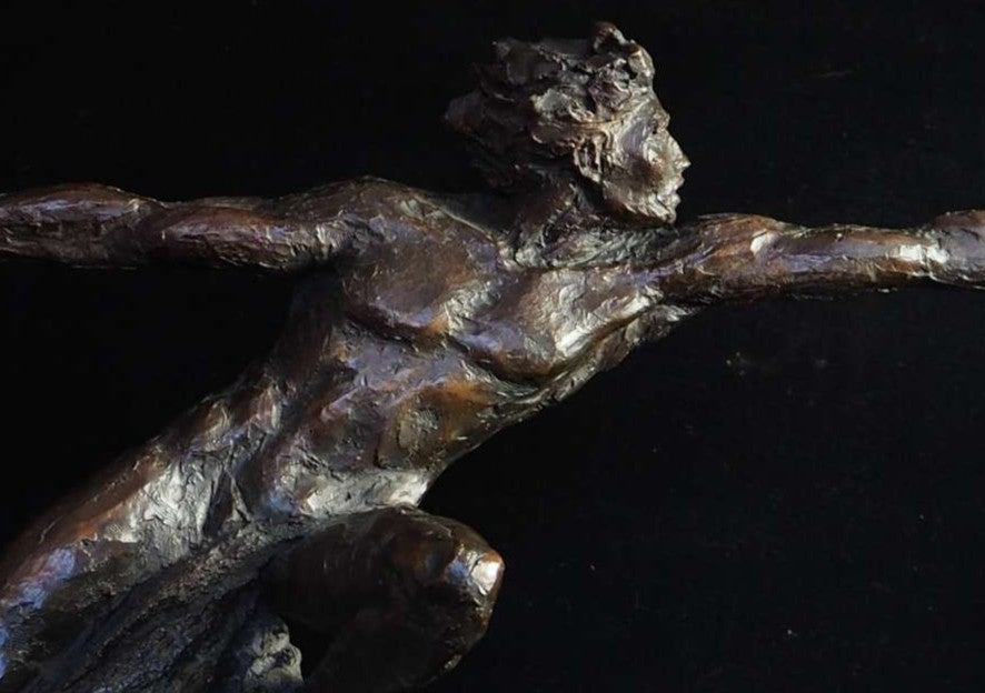 Bronze figurative sculpture by Eve Shepherd showing a dynamic human figure lunging forward with outstretched arms, balanced on a textured base, capturing tension, desire, and suspended movement against a dark background.