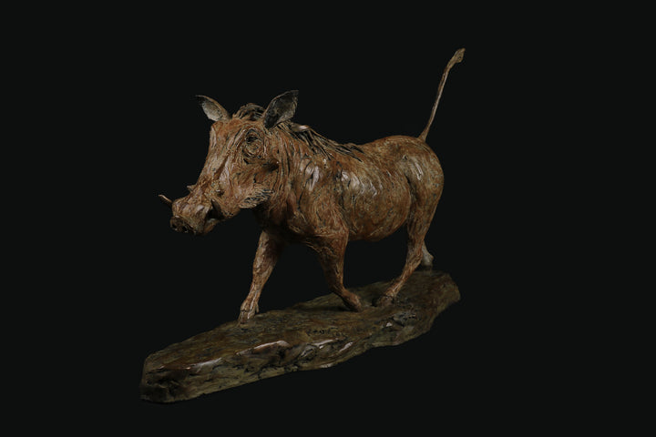 Bronze sculpture of a warthog mid-stride, with textured surface detailing and raised tail, mounted on a naturalistic base