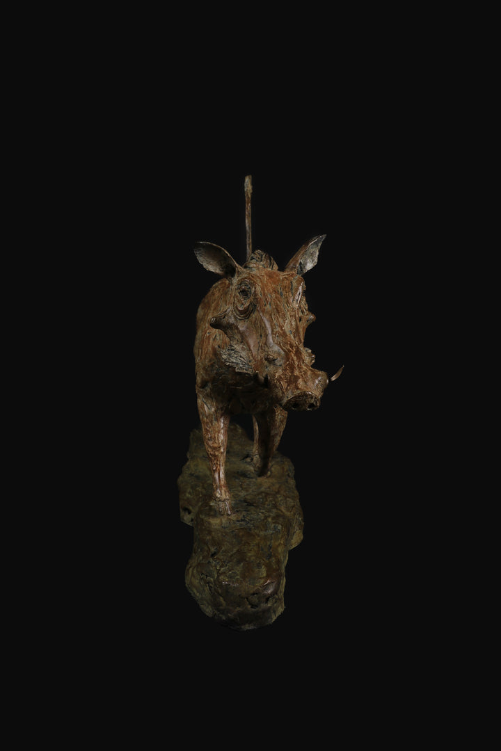 Bronze sculpture of a warthog mid-stride, with textured surface detailing and raised tail, mounted on a naturalistic base