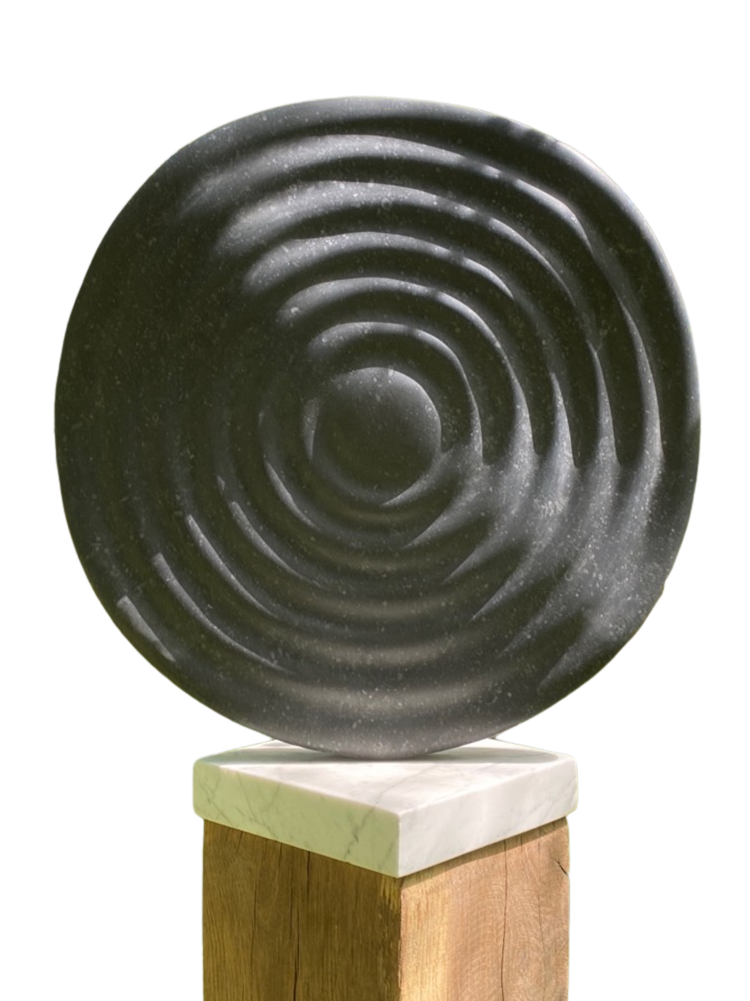 Circular abstract sculpture Wavelet – 2025 by Hamish Holman, carved in Kilkenny limestone with radiating ripple-like grooves across its dark stone surface, mounted on a white marble and oak plinth for indoor or outdoor display.