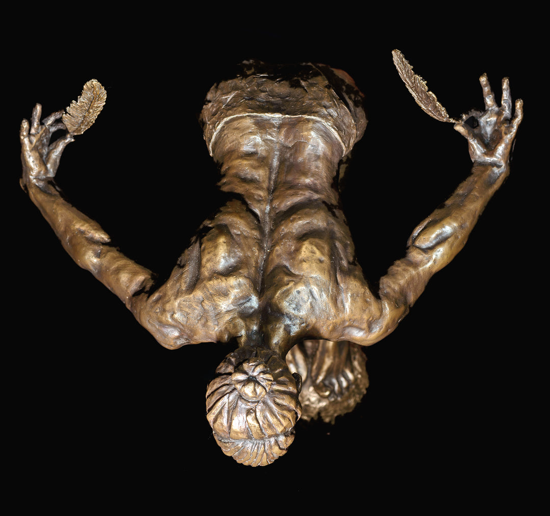 Ingenuity: Often thwarted by the shortsighted by Teresa Wells – a limited-edition bronze and steel sculpture depicting a poised, athletic female figure balanced on tiptoe atop a textured bronze sphere. The figure leans dramatically forward from the hips, arms extended behind and slightly upward, each hand delicately holding a detailed bronze feather. Muscular contours and tendons are rendered with lifelike precision, from the arched spine to the curled toes gripping the sphere. 