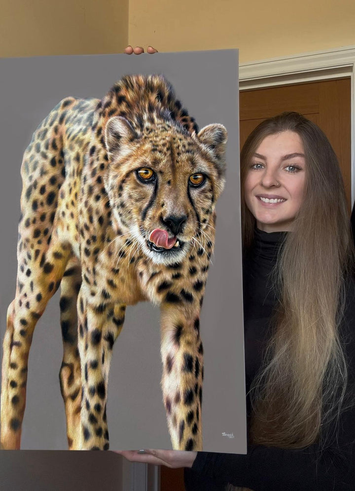 “Temptation” by Jemma Worsfold – a hyperrealistic coloured pencil drawing of a cheetah with golden eyes and tongue mid-lick, created on dark grey Clairfontaine Pastelmat. A one-off original capturing power, beauty, and instinct.