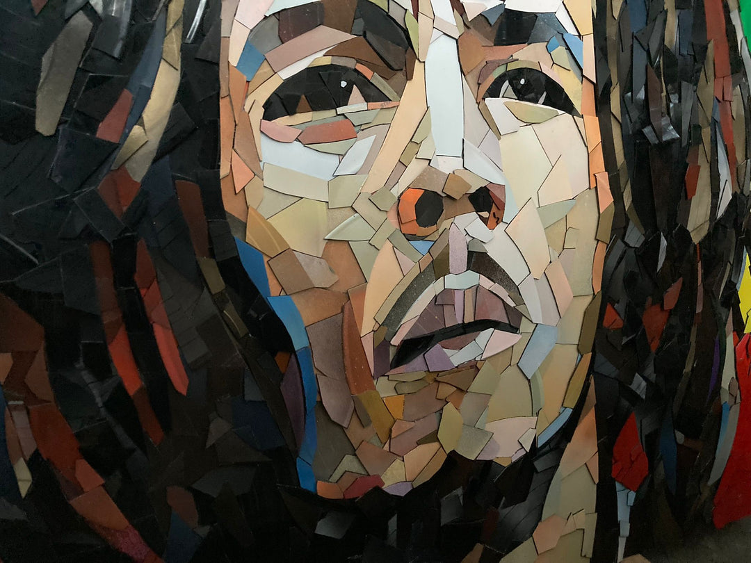 Ed Chapman Mosaic portrait of Bob Marley constructed from carefully cut fragments of reclaimed vinyl records, forming a highly detailed face with layered tonal variation and visible record grooves, set against a bold Rastafarian colour background that contrasts warm skin tones with strong graphic colour blocks and a textured, light-responsive surface.