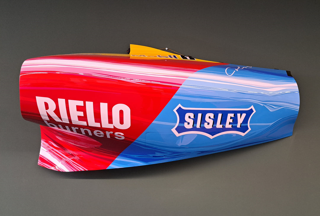 Custom-painted Formula 1 car sidepod with bold red, blue, and pink design featuring Riello and Sisley branding.
