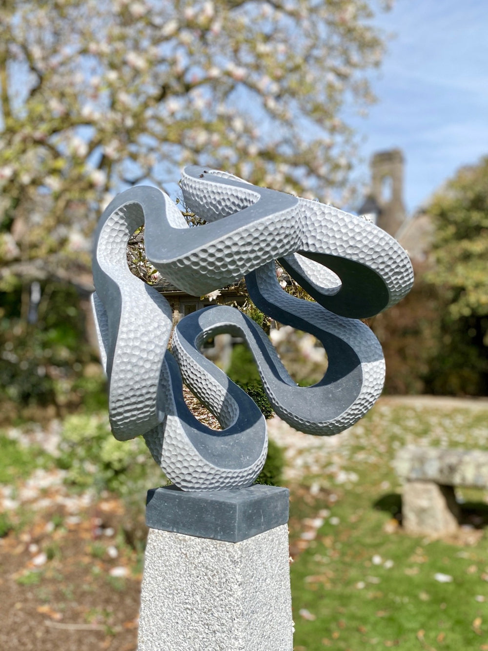 Abstract stone sculpture Wiggle – 2025 by Hamish Holman, carved in dark grey Kilkenny limestone with an interwoven looping form, combining smooth flowing curves with textured hand-carved dimples, dynamic and playful, mounted on a stone plinth.