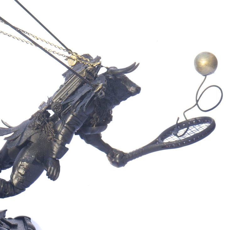A steampunk sculpture featuring winged minotaur figures assembled from broken toys, brass clock parts, wood offcuts and metal components, all finished in a dark bronze patina. The figures appear in playful motion, including one holding a tennis racket, set on an ornate mechanical base with gears and cogs.