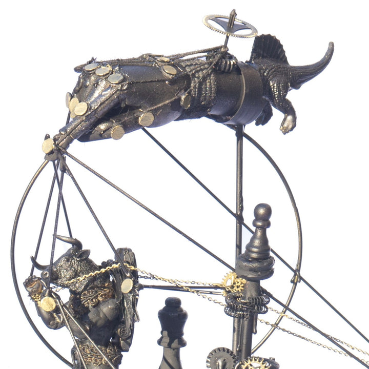 A steampunk sculpture featuring winged minotaur figures assembled from broken toys, brass clock parts, wood offcuts and metal components, all finished in a dark bronze patina. The figures appear in playful motion, including one holding a tennis racket, set on an ornate mechanical base with gears and cogs.