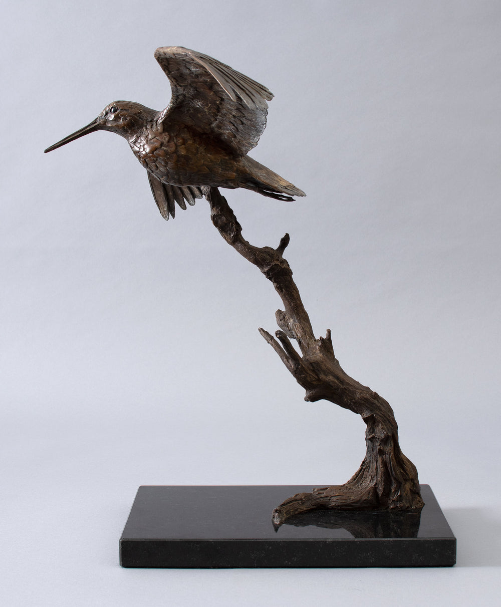 Close-up of a bronze bird sculpture with wings extended in flight, detailed feather texture and elongated beak


