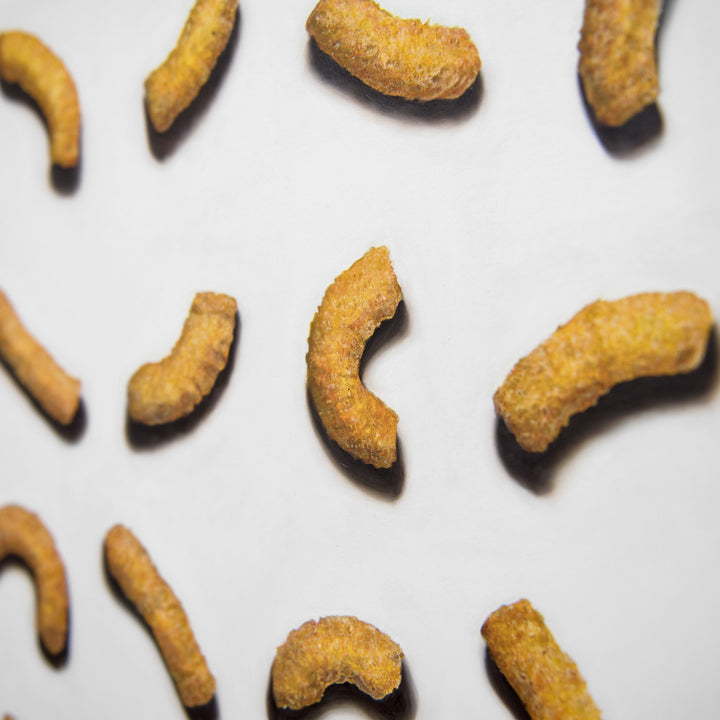 Baked Wotsits 16.5g Pack 82 KCal, 2024 by Simon Taylor – photorealistic oil painting on linen depicting rows of curved orange corn snacks arranged against a white background, each crisp rendered with detailed texture, granular surface and soft shadow.