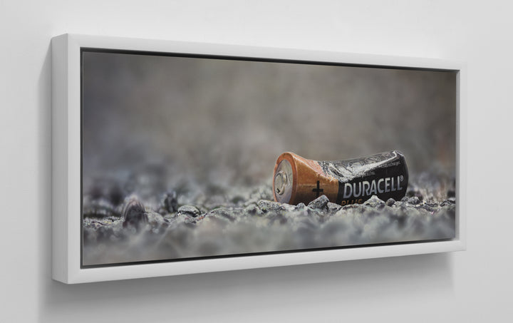Simon Taylor, YOU LEFT ME POWERLESS (Original), oil and acrylic on aluminium, 25 x 60cm – photorealist painting of a discarded Duracell battery lying on grey gravel, rendered with hyperreal precision.
