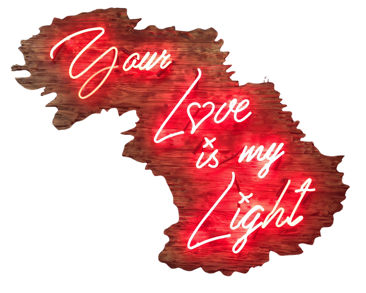 Neon artwork by Matthew Bracey in warm white script reading “Your Love is my Light,” mounted on a uniquely contoured, deep red wood panel shaped like a stylised landscape or abstract map. The word “Love” is stylised with a heart-shaped “o,” glowing against rich wood grain and glowing red backlighting.