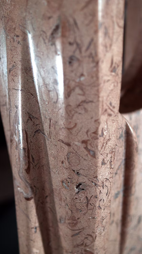 A tall abstract stone sculpture with two inward-facing vertical spires joined at the base, carved in contrasting smooth and textured Purbeck stone, mounted on a dark granite base.