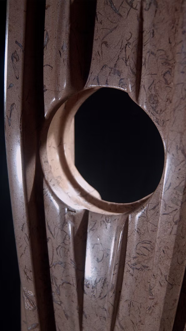 A tall abstract stone sculpture with two inward-facing vertical spires joined at the base, carved in contrasting smooth and textured Purbeck stone, mounted on a dark granite base.