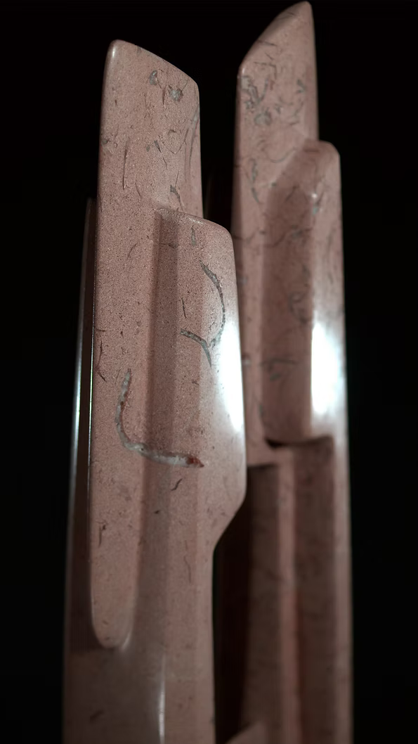 A tall abstract stone sculpture with two inward-facing vertical spires joined at the base, carved in contrasting smooth and textured Purbeck stone, mounted on a dark granite base.