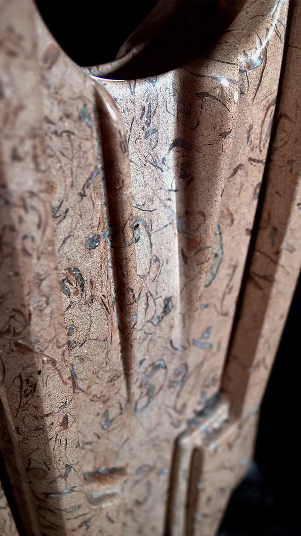 A tall abstract stone sculpture with two inward-facing vertical spires joined at the base, carved in contrasting smooth and textured Purbeck stone, mounted on a dark granite base.