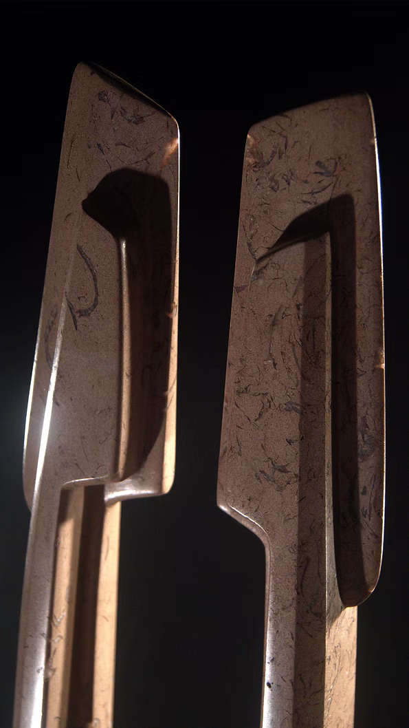 A tall abstract stone sculpture with two inward-facing vertical spires joined at the base, carved in contrasting smooth and textured Purbeck stone, mounted on a dark granite base.