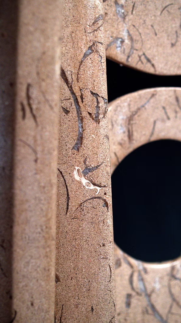 A tall abstract stone sculpture with two inward-facing vertical spires joined at the base, carved in contrasting smooth and textured Purbeck stone, mounted on a dark granite base.