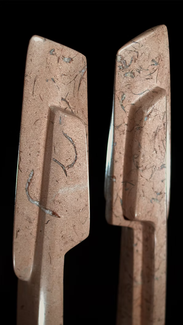 A tall abstract stone sculpture with two inward-facing vertical spires joined at the base, carved in contrasting smooth and textured Purbeck stone, mounted on a dark granite base.