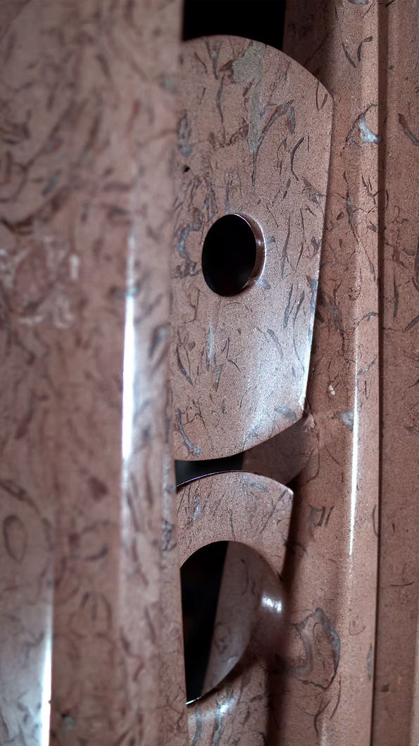 A tall abstract stone sculpture with two inward-facing vertical spires joined at the base, carved in contrasting smooth and textured Purbeck stone, mounted on a dark granite base.