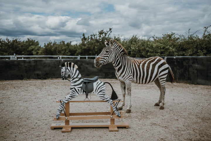 Hand-painted wooden rocking zebra with black leather saddle, mounted on a dark oak safety stand.
