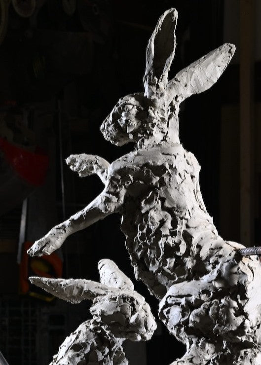 ‘Boxing Hares’ by Hamish Mackie, a limited-edition bronze wildlife sculpture depicting two hares leaping and boxing in mid-air during their characteristic springtime courtship behaviour. The dynamic composition captures their extended limbs, twisting bodies and expressive movement, with richly textured surfaces that convey the energy of the original hand-modelled clay. Photograph shows the original clay sculpture prior to bronze casting.