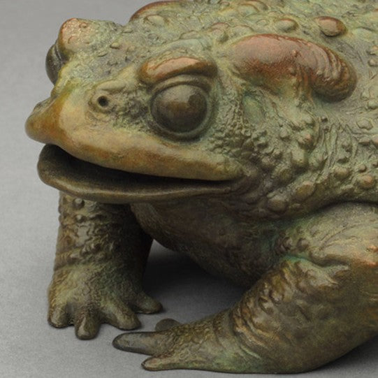Bronze sculpture of a small toad in a seated, alert posture, detailed textured skin with raised bumps and a natural green–bronze patina.