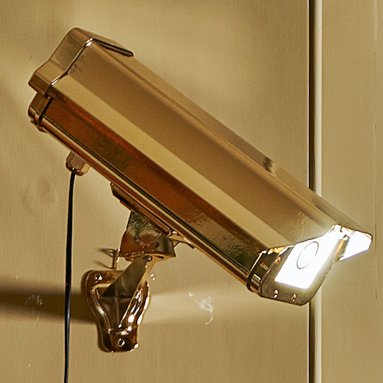 “CCTV Lights – Wall Hung” by Ben Rousseau – a gold-plated light sculpture transforming a surveillance camera into a striking wall-mounted LED artwork. A playful yet luxurious statement merging art, technology, and illumination.

