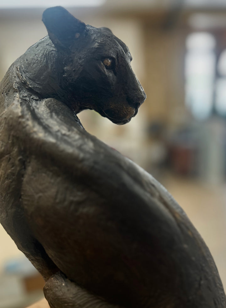 Sculpted panther by Lucy d’Auvergne in dark cold cast bronze with a sleek, muscular form and subtle textured surface, poised on a solid oak plinth against a deep shadowed background.