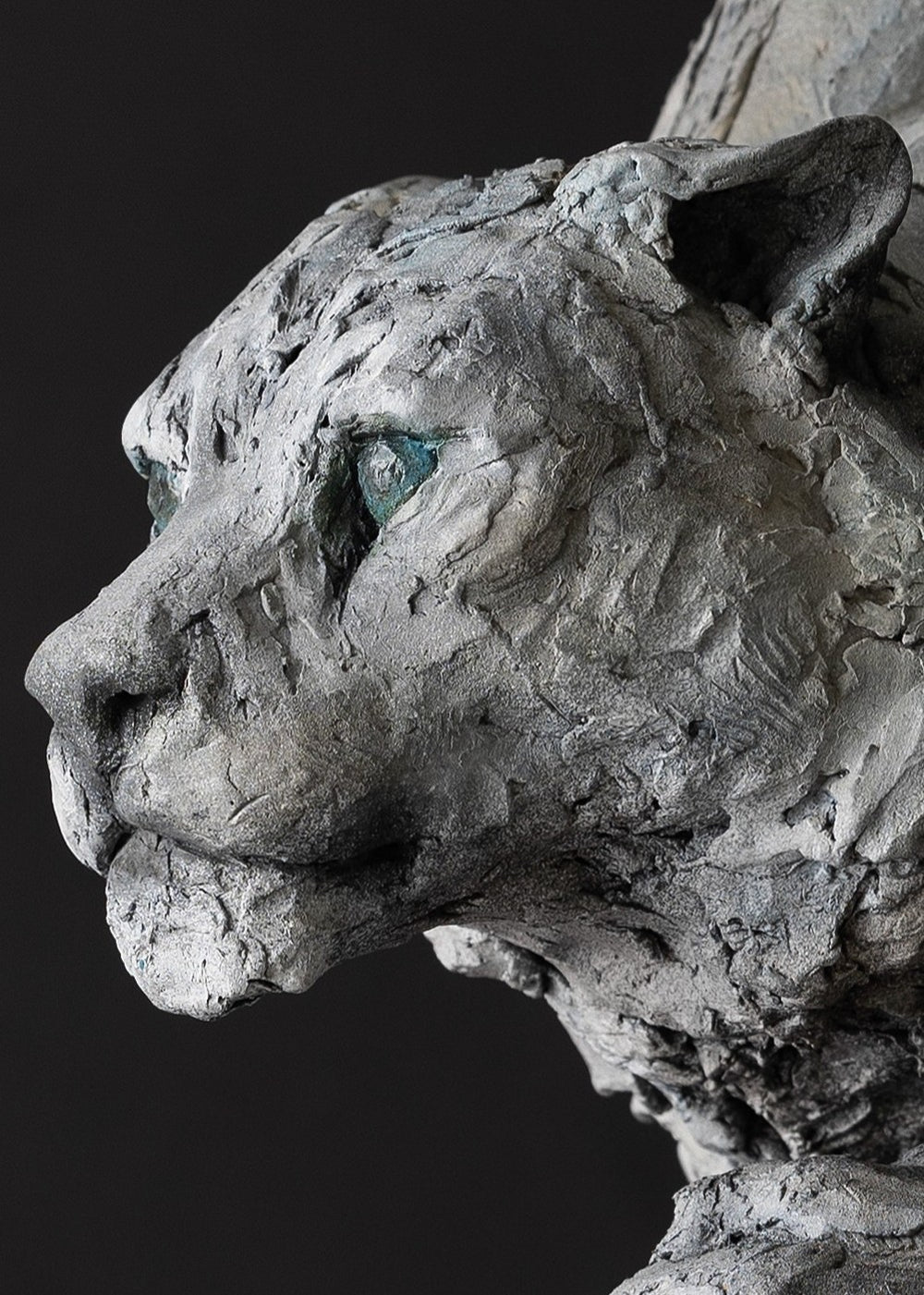 Sculpture of a stalking snow leopard by Lucy d’Auvergne, created in cast slate with raw earth pigments, showing a powerful crouched pose with textured grey and earthy tones, green eyes, and mounted on a granite base.