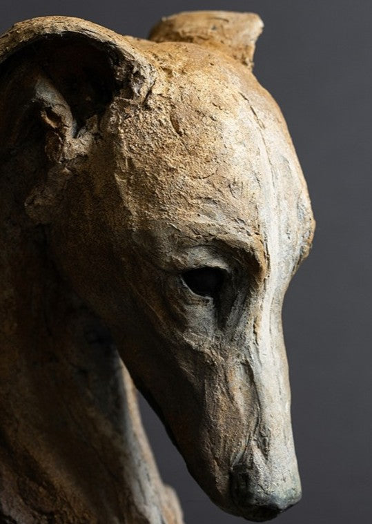 Sculpture of a contemplative dog’s head by Lucy d’Auvergne, cast in slate with raw earth pigments creating warm ochre and umber tones with deep charcoal shadows, mounted on a polished granite base.