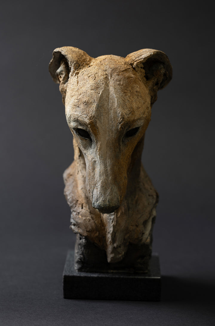 Sculpture of a contemplative dog’s head by Lucy d’Auvergne, cast in slate with raw earth pigments creating warm ochre and umber tones with deep charcoal shadows, mounted on a polished granite base.