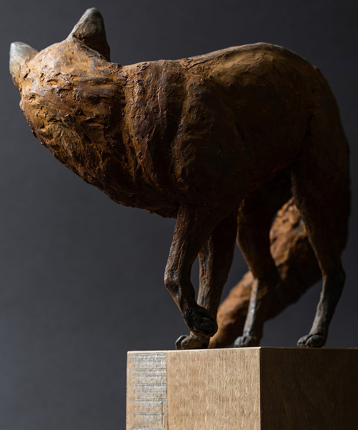 Sculpture of a young fox by Lucy d’Auvergne, cast in cold cast iron with warm earthy brown patina, shown standing alert and turning its head, mounted on a natural oak plinth.