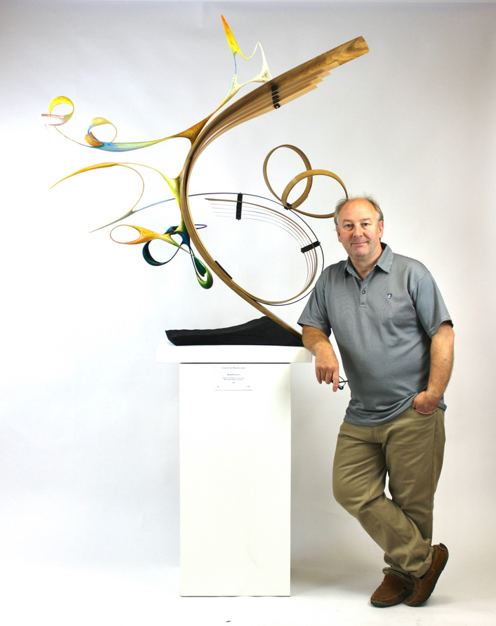 Freedom by Mark Purllant, an award-winning one-off mixed media sculpture in carved and steam-bent English oak with painted sculptural forms, maple veneer, ebony, and brass details, mounted on a scorched oak base with flowing, dynamic curves in yellow, blue, orange, and green.