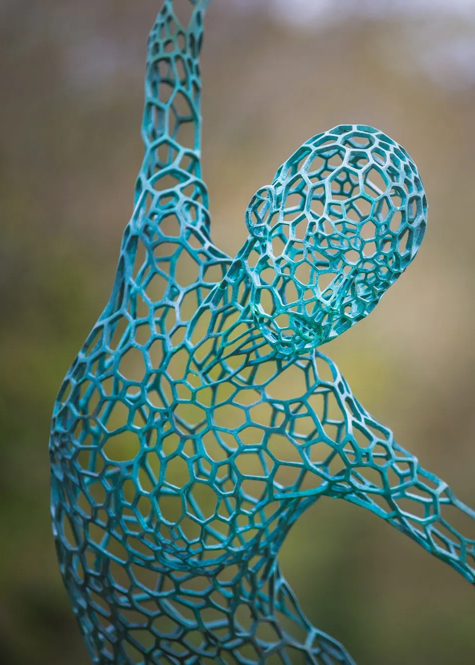 Simon Gudgeon bronze sculpture Athena featuring an elegant open lattice female form with blue green patina displayed within a landscaped outdoor garden setting.