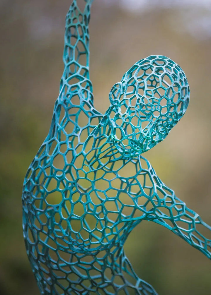 Simon Gudgeon bronze sculpture Athena featuring an elegant open lattice female form with blue green patina displayed within a landscaped outdoor garden setting.